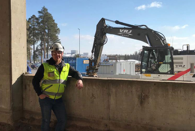 Kuva Hartelan työntekijästä työmaalla, jonka taustalla näkyy kaivinkone