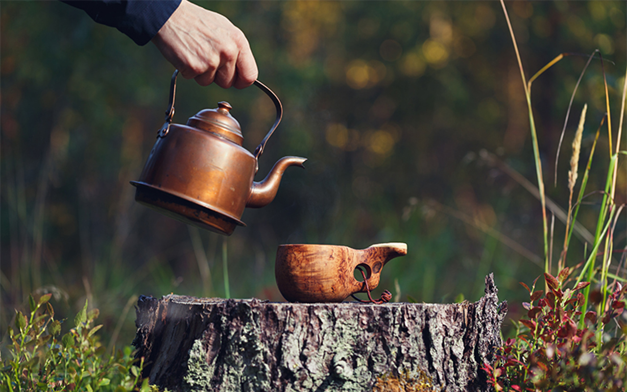 Kuksa kannon päällä metsässä, johon kaadetaan kahvia teräspannusta.