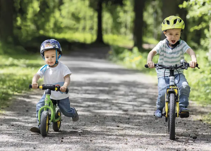 Valokuva, jossa kaksi lasta pyöräilee hiekkatiellä kypärät päässä