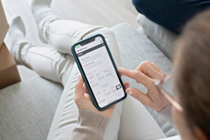 Nainen istuu sohvalla ja katsoo kännykkäänsä