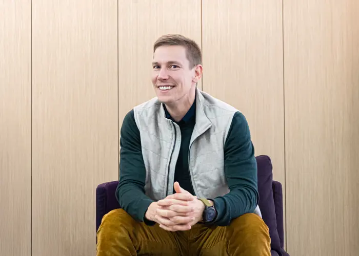 Lari Mallius istuu tuolilla ja hymyilee kameralle